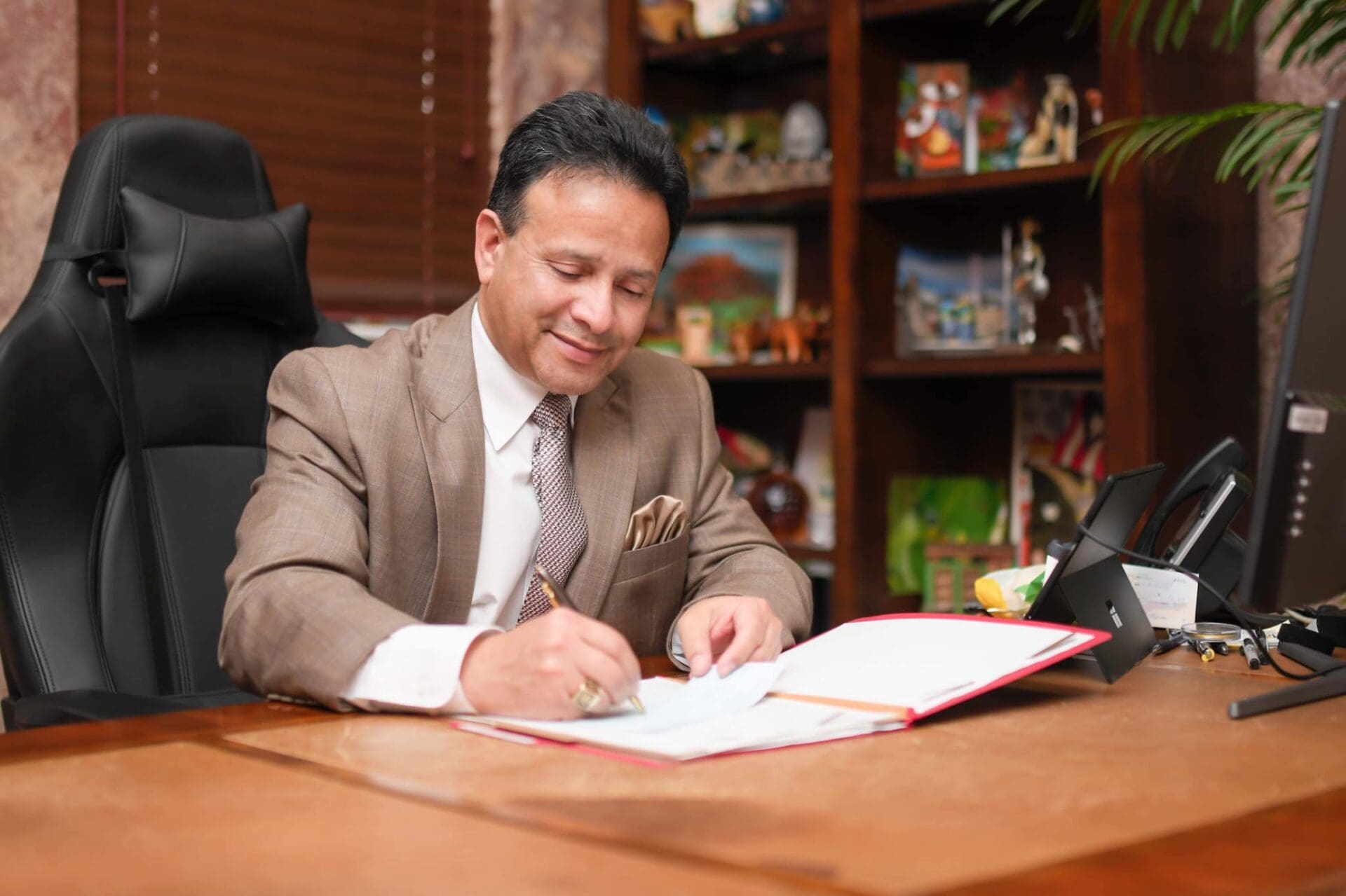 A man in suit and tie sitting at table writing on paper.